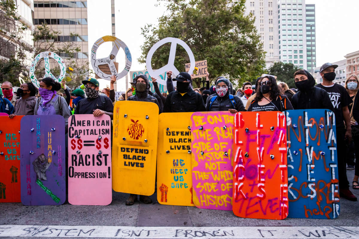 Protesters stand behind a vibrantly colored rainbow of homemade sheilds