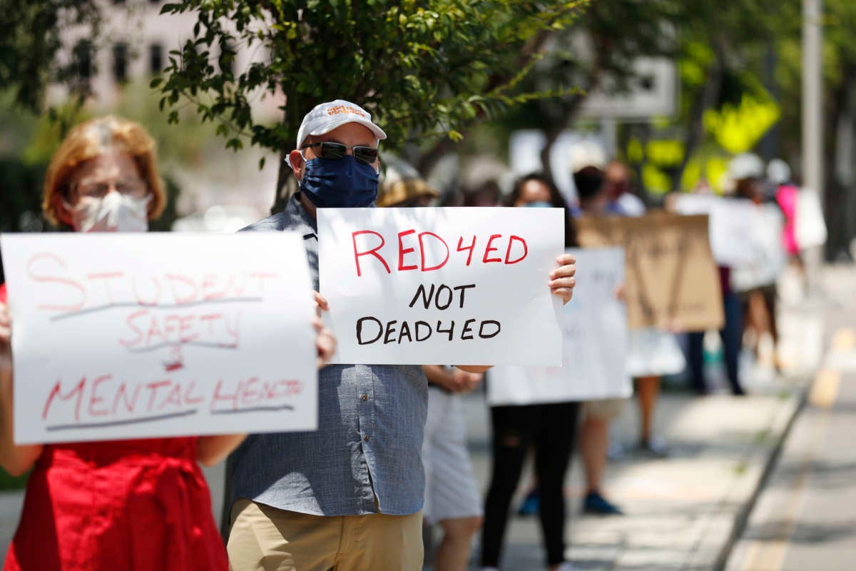 A teacher holds a sign reading "RED 4 ED NOT DEAD 4 ED" during a socially distanced protest