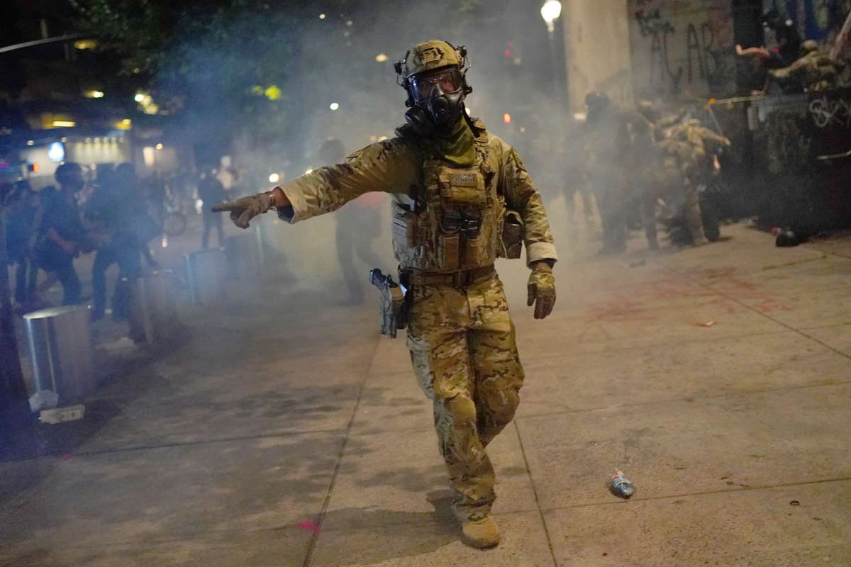 A federal goon points as people scatter from the teargas surrounding them