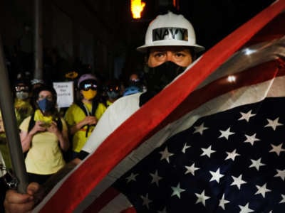 A man in a hard hat with "NAVY" written on it waves an upside-down U.S. Flag