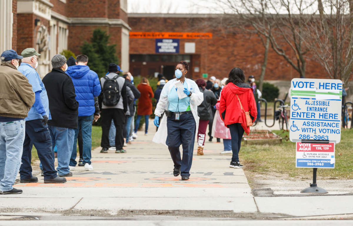 A woman hands out surgical masks to people standing in line to vote in Wisconsin's primary election on April 7, 2020, at Riverside High School in the city of Milwaukee.