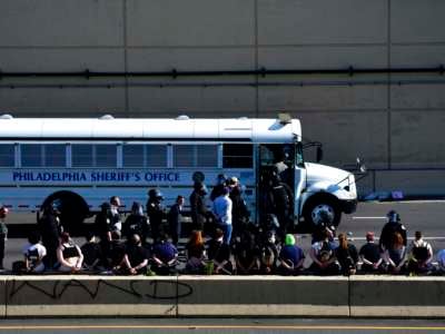 Arrested protesters stand and sit on a barrier of the Vine Street Expressway after police shot tear gas to disperse the crowd on June 1, 2020, in Philadelphia, Pennsylvania.