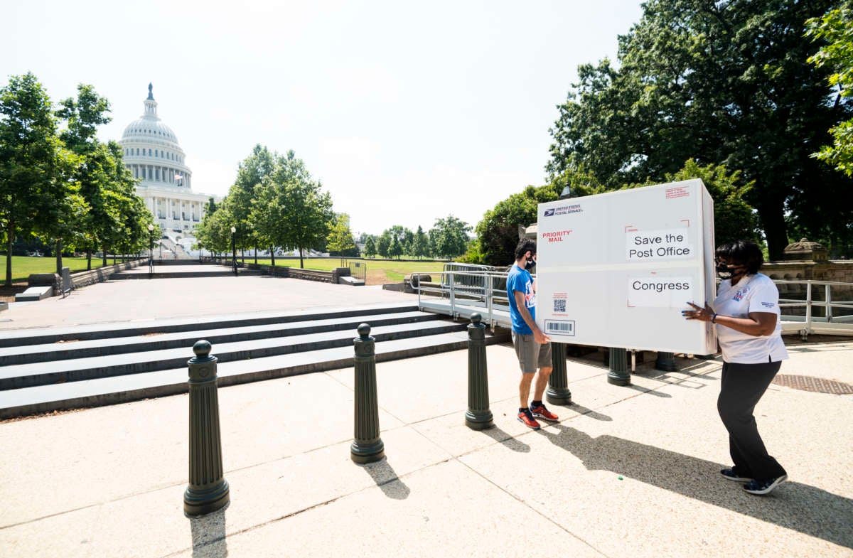 From left, Garrett Schaffel, and Judy Beard, American Postal Workers Union national legislative and political director, carry a Priority Mail box towards the Capitol for a photo-op on Tuesday, June 23, 2020.