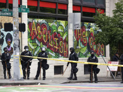 Seattle Police stand in front of graffiti that reads "abolish the cops" and block the entrance to the Capitol Hill Organized Protest (CHOP) after clearing it and retaking the department's East Precinct in Seattle, Washington, on July 1, 2020.