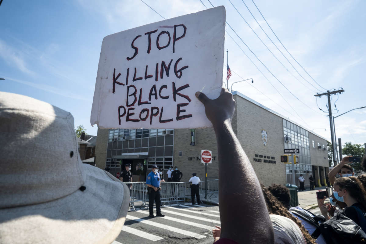 A protester holds a sign that says, "Stop Killing Black People" as the crowd stands in front of the 111th New York Police Department Precinct with police officers looking on during the Black Lives Matter protest in Bayside, Queens, NYC, on August 1, 2020.