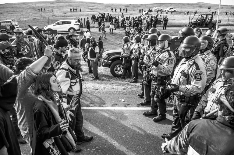 Arrested on October 10 and 22, 2016 and again on January 16, 2017, Water Protector Olive Bias (front, left) stands singing in prayer on October 27, another day of mass arrests and brutality.