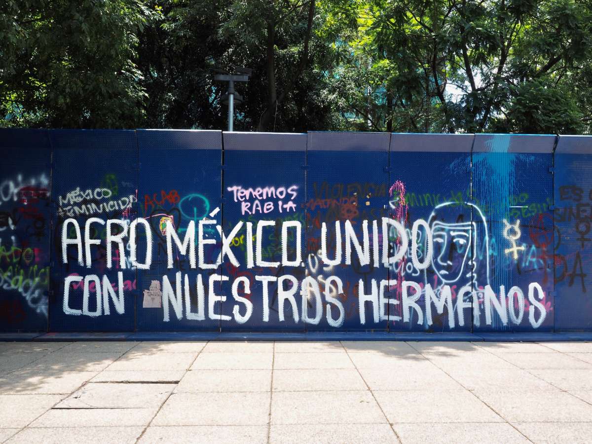 A blue wall is tagged with "Afro Mexico United With Our Brothers," in Spanish