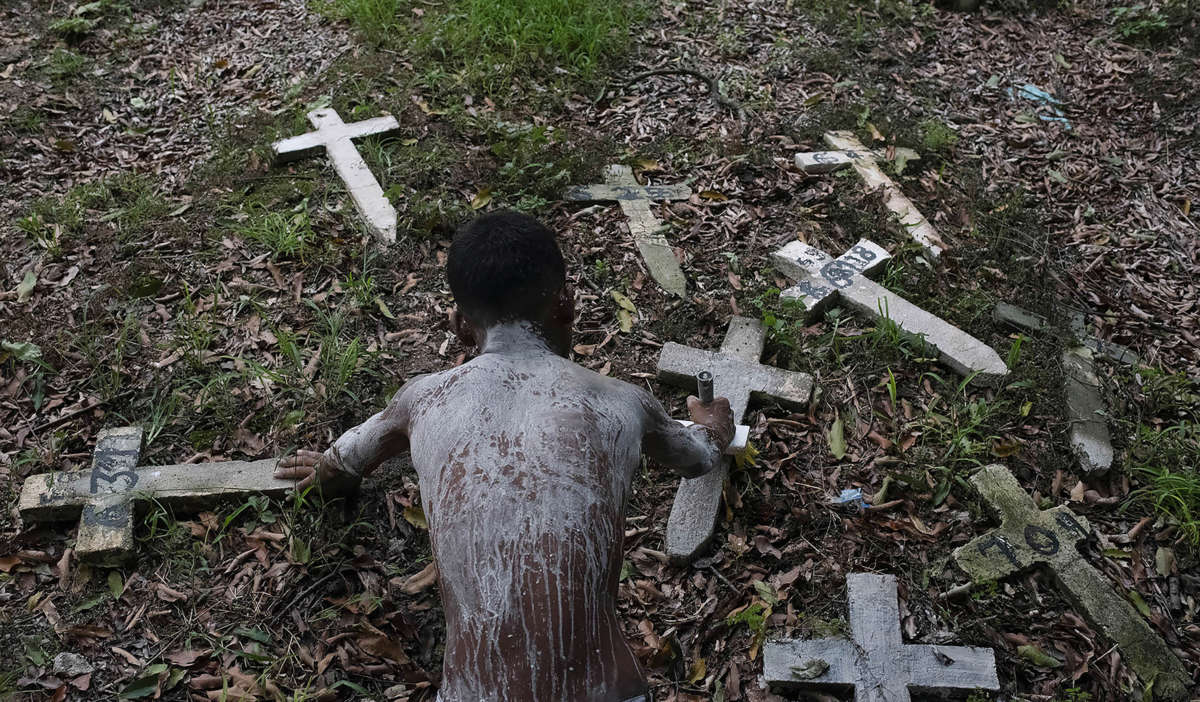 Josué Vicente Pereira paints crosses white and earns 0.50 centavos (less than 10 U.S. cents) per cross. He has limewash paint on his back because he must go inside burial drawers to paint in the Caju Cemetery, in Rio de Janeiro, Brazil.