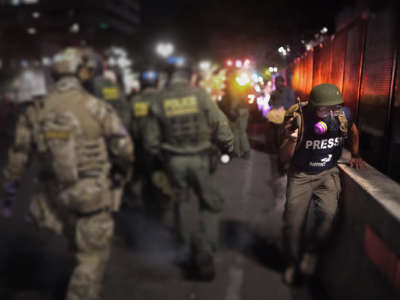 A journalist runs past federal officers during a nighttime protest