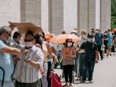 Masked people stand in a line outdoors while waiting for food donations