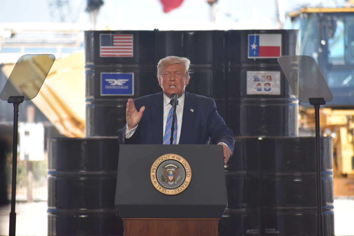 Donald Trump speaks while standing in front of oil barrels