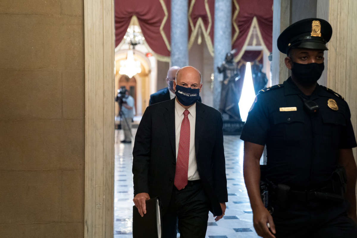 Louis DeJoy walks down a hallway behind a cop