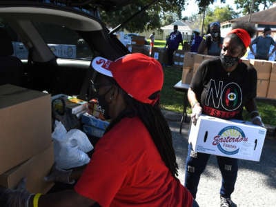 Two masked women load boxes of food into a car's trunk