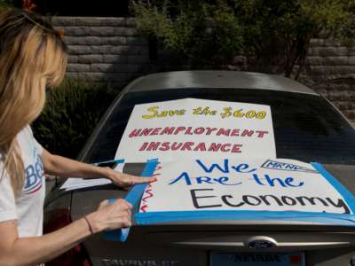 A masked woman tapes signs reading "Save the $600 unemployment insurance" and "We are the economy" to her car