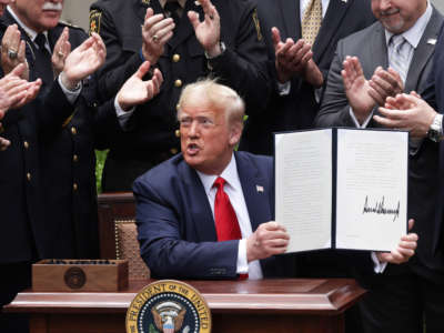 Surrounded by members of law enforcement, President Trump holds up an executive order he signed on “Safe Policing for Safe Communities” during an event in the Rose Garden at the White House, June 16, 2020, in Washington, D.C.