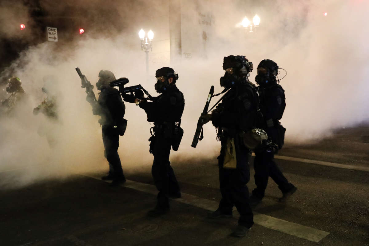 Cops walk down a street fogged with the tear gas they shot at peaceful protesters