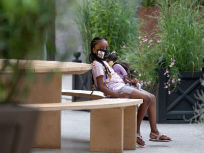 A girl holds a doll while sitting in near plants