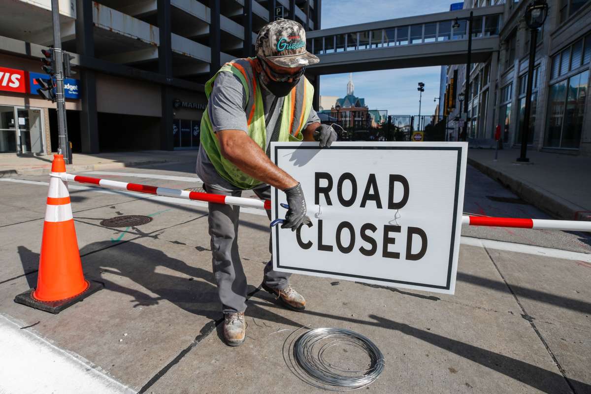 A worker affixes a "ROAD CLOSED" sign to a barricade