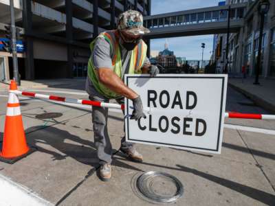 A worker affixes a "ROAD CLOSED" sign to a barricade