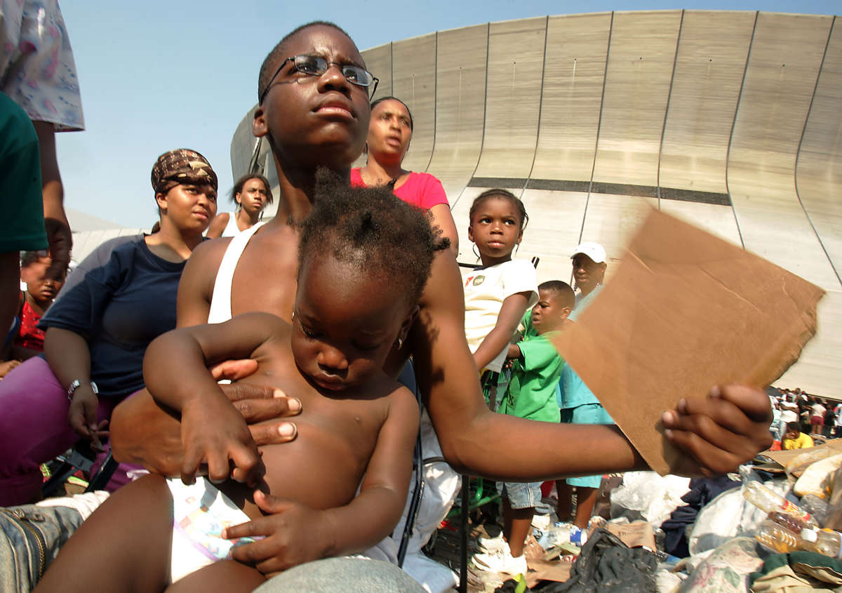 A boy fans himself and a baby he's holding as he waits with others outside the Superdome