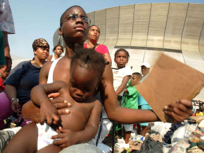 A boy fans himself and a baby he's holding as he waits with others outside the Superdome