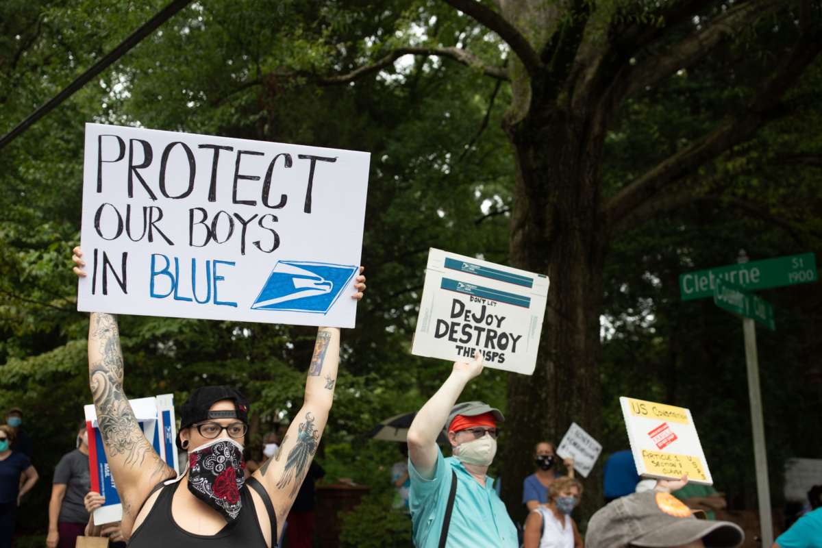 A protester holds a sign reading "PROTECT OUR BOYS IN BLUE" with a usps logo on it