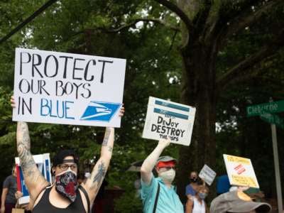 A protester holds a sign reading "PROTECT OUR BOYS IN BLUE" with a usps logo on it