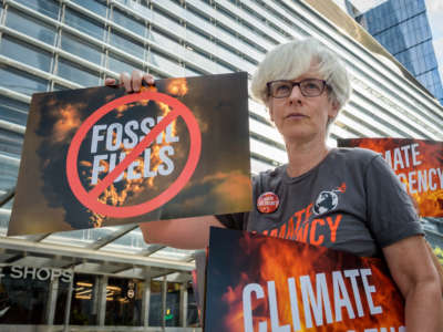 A climate activist holds signs that read "Fossil Fuel" with a large red "no" symbol over it