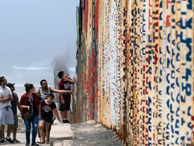 A family walks beside the us/mexico border wall on the beach