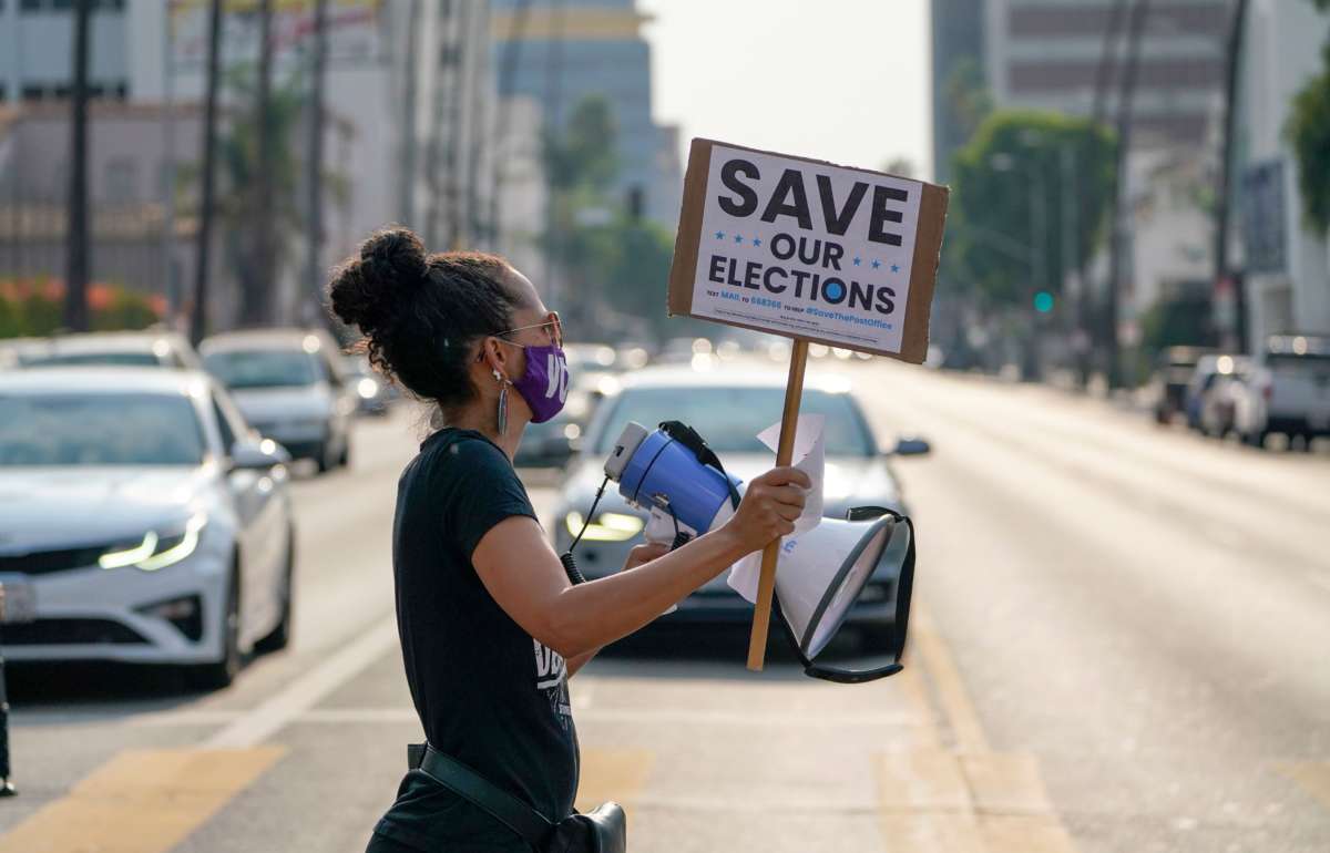 A protester crosses a street holding a sign reading "SAVE OUR ELECTIONS"