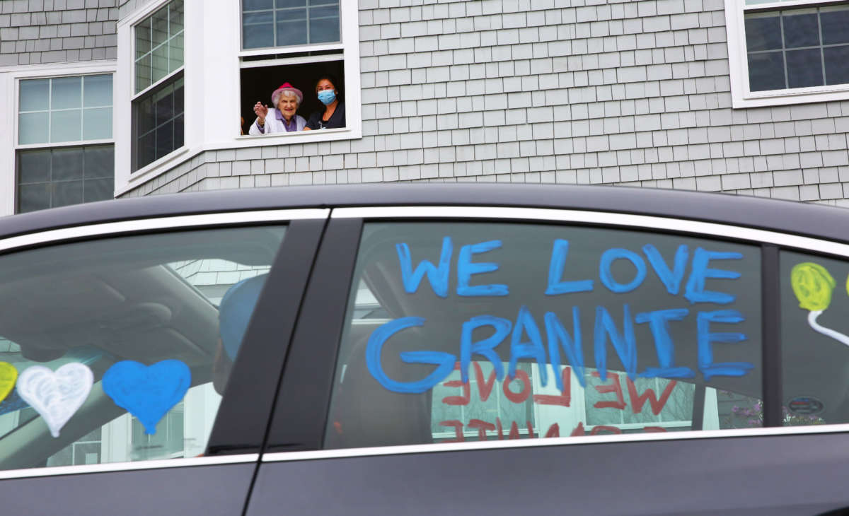 Eleanor Dittmer, joined in the window by nurse's aide Courtney Nadeau at the Harriett and Ralph Kaplan Estates in Peabody, Massachusetts, has a drive-by birthday party in the parking lot of the facility on April 26, 2020.