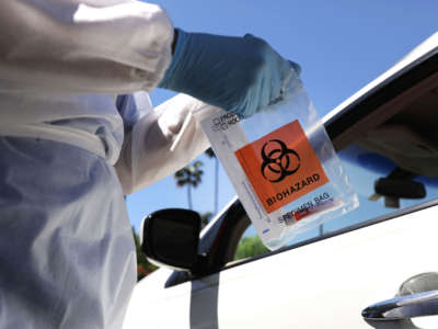 A healthcare worker prepares to hand a test kit to a motorist at a drive-in COVID-19 testing center on August 11, 2020, in Los Angeles, California.