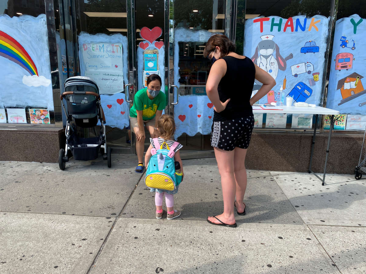 a masked daycare teacher greets a student