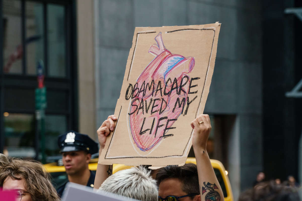 A person holds a sign reading "OBAMACARE SAVED MY LIFE" during an outdoor pre-covid protest