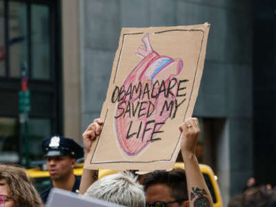 A person holds a sign reading "OBAMACARE SAVED MY LIFE" during an outdoor pre-covid protest