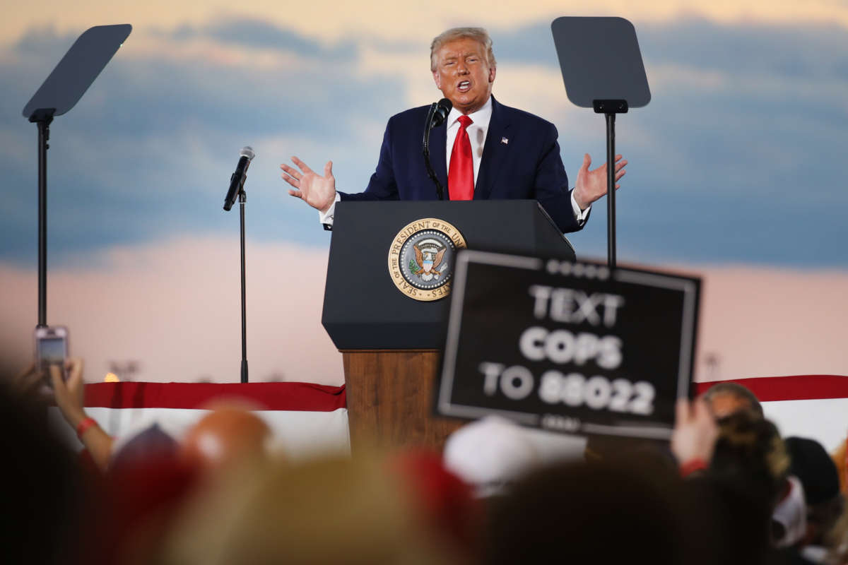 Donald Trump speaks at a podium while a supporter holds a sign about cops in the foreground