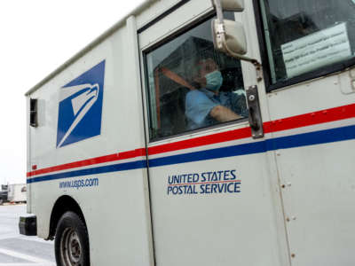 A USPS mail worker wearing a mask is seen driving between houses on August 13, 2020, in Ventnor City, New Jersey.