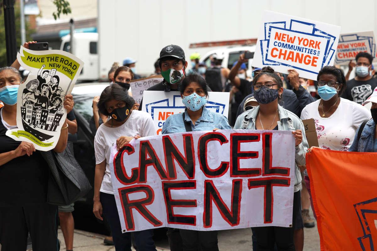 Masked protesters hold a large sign reading "CANCEL RENT"