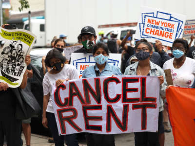 Masked protesters hold a large sign reading "CANCEL RENT"