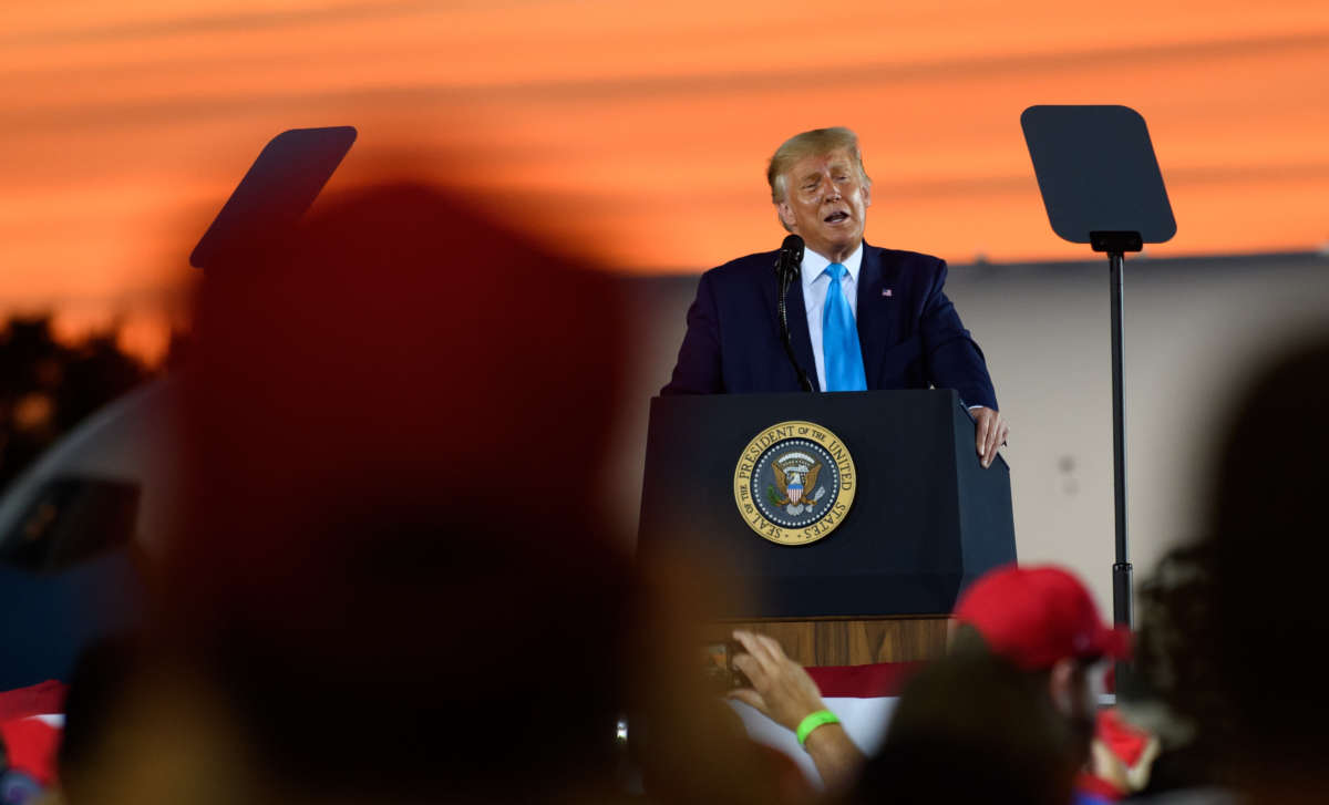 Donald Trump, sweating profusely and matching the orange sunset behind him, speaks at a podium