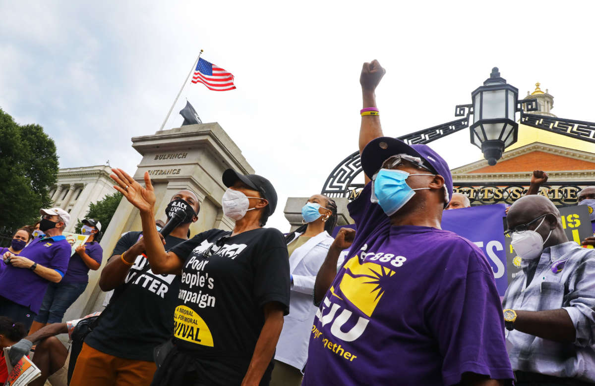 As activist Savina Martin, center, with the People's Forum, speaks, Anthony Meeks, with SEIU Local 888, throws up a fist during an SEIU members rally in front of the State House in Boston on "a day of reckoning" for Black Lives on July 20, 2020.