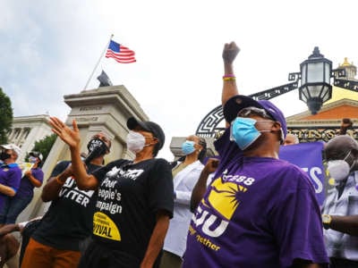 As activist Savina Martin, center, with the People's Forum, speaks, Anthony Meeks, with SEIU Local 888, throws up a fist during an SEIU members rally in front of the State House in Boston on "a day of reckoning" for Black Lives on July 20, 2020.