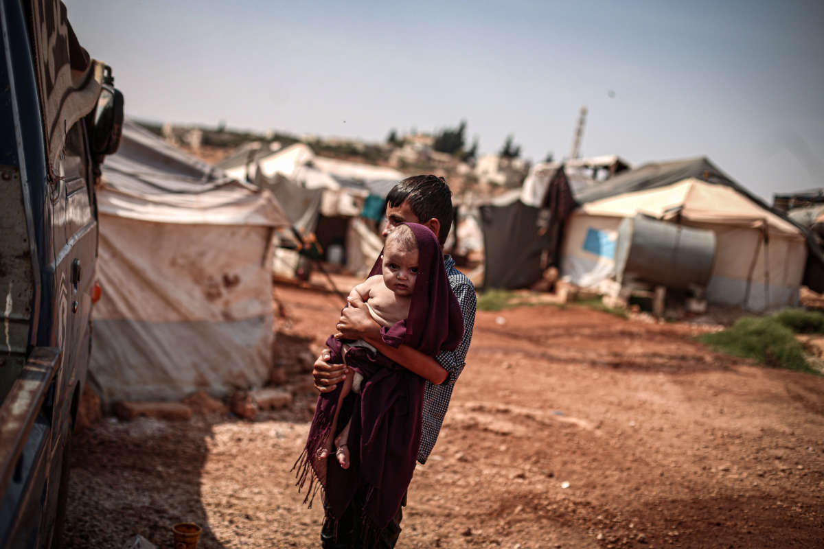 A Syrian youth holds a baby as he covers the baby's head with a fabric to protect him from sun during hot weather at a refugee camp where displaced Syrians shelter in Idlib, Syria, on September 1, 2020.