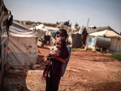 A Syrian youth holds a baby as he covers the baby's head with a fabric to protect him from sun during hot weather at a refugee camp where displaced Syrians shelter in Idlib, Syria, on September 1, 2020.