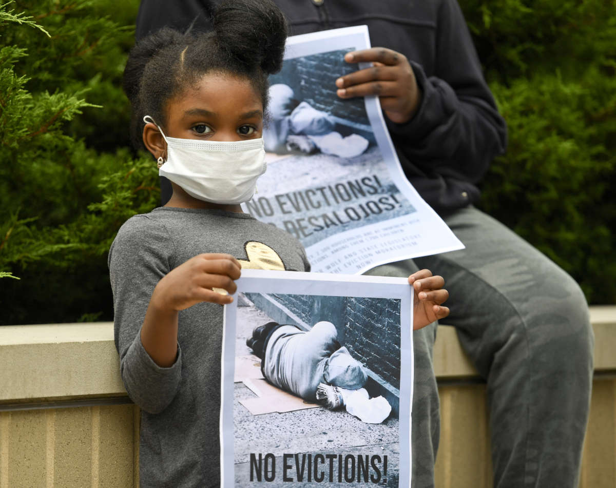 A little girl in a face mask holds a sign reading "NO EVICTIONS!"