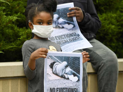 A little girl in a face mask holds a sign reading "NO EVICTIONS!"