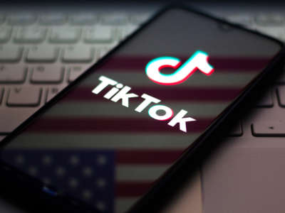 The TikTok logo is seen displayed on a smartphone with an American flag reflected in it.