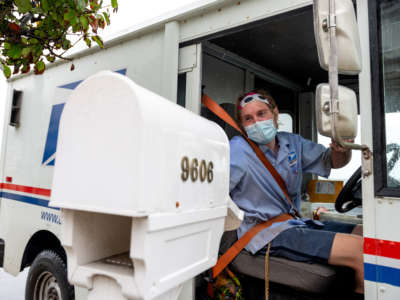 A USPS worker wearing a mask puts envelopes in a mailbox on August 13, 2020, in Ventnor City, New Jersey.