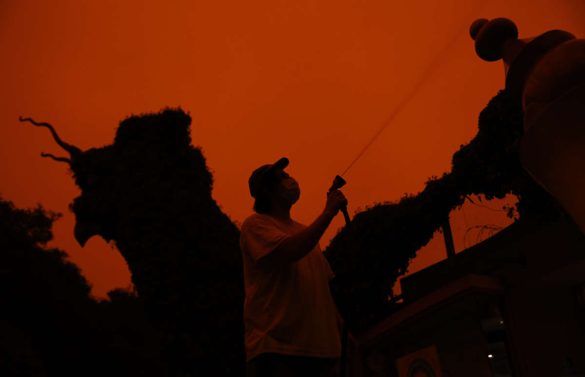 A custodian cleans the entrance of Children's Fairyland as the sky burns a dark orange hue because of wildfire smoke in the atmosphere, September 9, 2020, in Oakland, California.