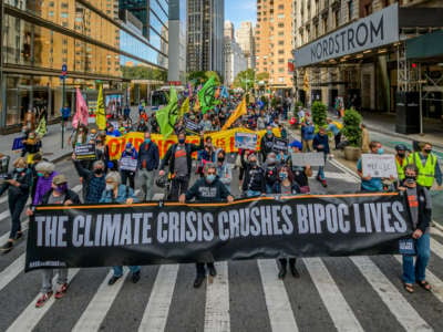 people march behind a banner reading "THE CLIMATE CRISIS CRUSHES BIPOC LIVES" during a protest